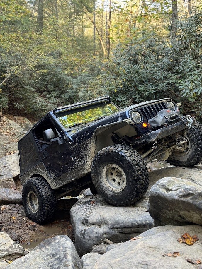 Black Jeep climbing a rocky obstacle in the woods