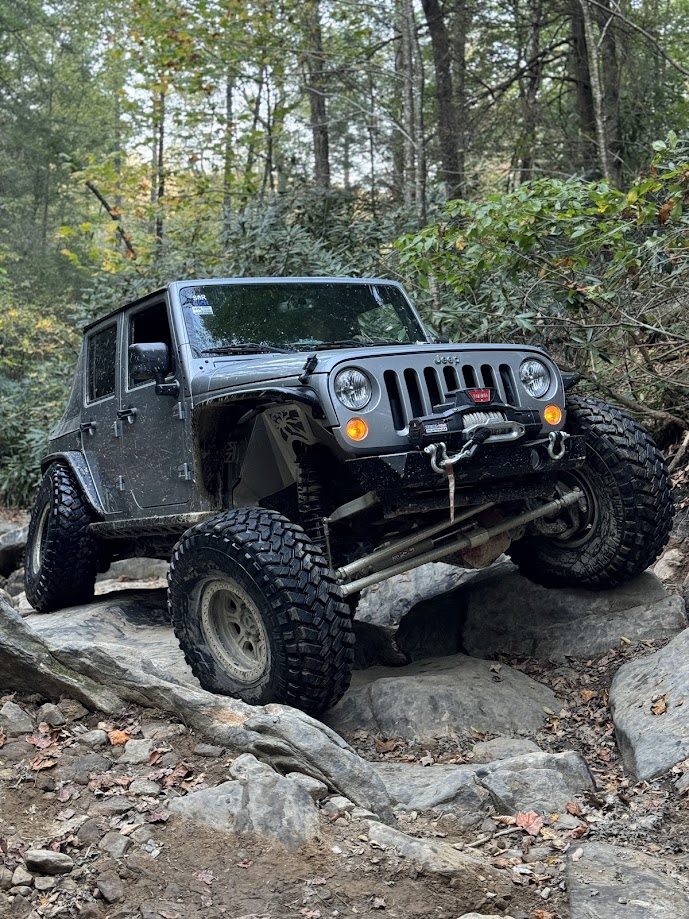 Modified gray Jeep climbing over large rocks