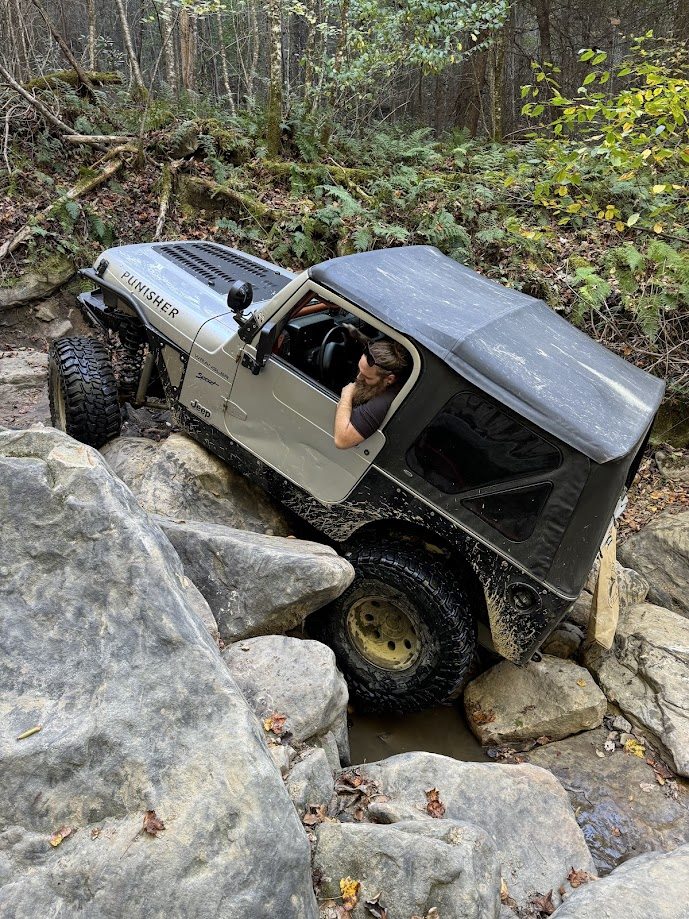 Modified Jeep navigating boulders on a wooded trail